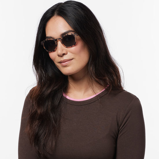 Woman wearing sunglasses and a brown long-sleeve shirt on a white background