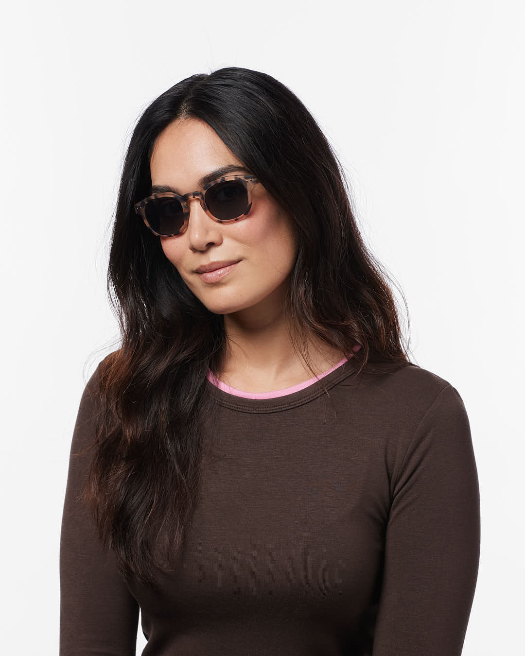 Woman wearing sunglasses and a brown long-sleeve shirt on a white background