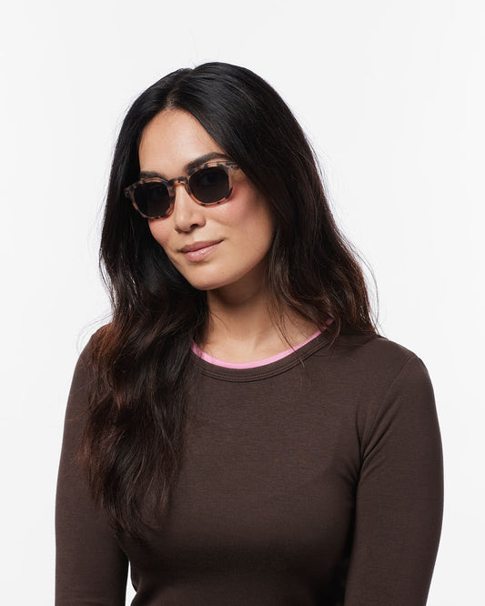 Woman wearing sunglasses and a brown long-sleeve shirt on a white background
