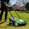 Person using a green and black lawn mower on a grassy area with a house and trees in the background.