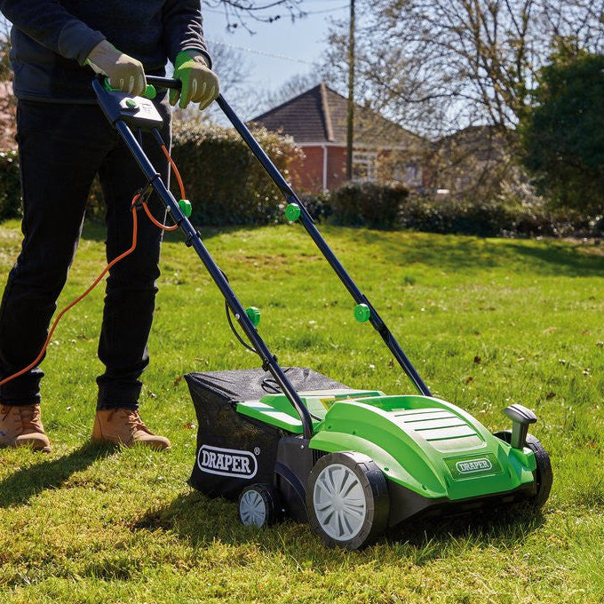 Person using a green and black lawn mower on a grassy area with a house and trees in the background.